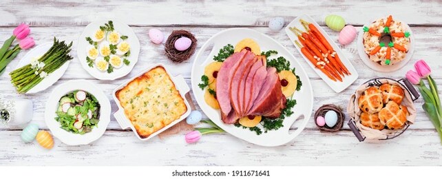 classic easter ham dinner. top down view table scene on a white wood banner background. ham, scalloped potatoes, eggs, hot cross buns, carrot cake and vegetables.