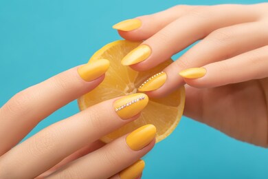 female hands with yellow nail design. yellow nail polish manicure. woman hands with yellow lemon on blue background. copy space