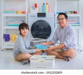asian father with his son is doing laundry in washing machine at home together for family housework togetherness concept.