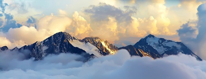alpine landscape with peaks covered by snow and clouds. banner. panorama