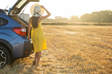 young woman driver in yellow summer dress and straw hat standing near a car enjoying warm summer day at sunset. travel and vacation concept.