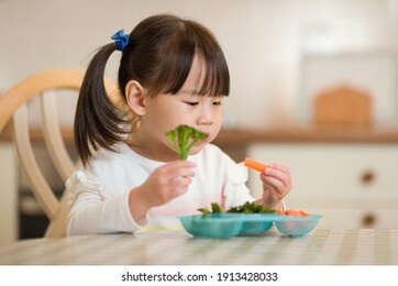 young girl eating fresh green vegetale against real kitchen background