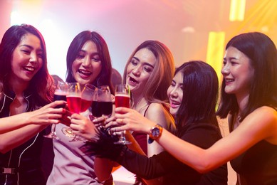 young people celebrating a party, drink and dance . group of friend toasting drinks while having fun at the disco club at night . friendship and nightlife concept .