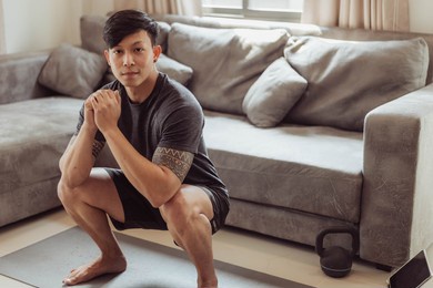 fit man in sportwear doing squat exercise at home. young asian man doing workout at home. home exercise in quarantine.