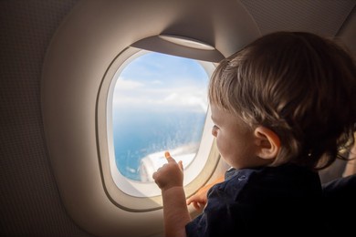 toddler looks at the ground through the porthole of a flying plane. travel with children