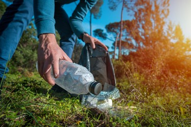 man cleaning-up the forest of plastic garbage. nature cleaning. volunteer picking up a plastic bottle in the woods. green and clean nature. plastic awareness activism and ecology concept