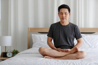 the male buddhist sitting on bed in the bedroom and doing meditation before sleeping time. idea for faith and trust in religion and calm of mind.
