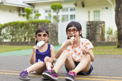 little girls  eating ice cream and sitting before their house
