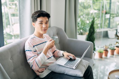 happy young man sitting at home, working on laptop computer