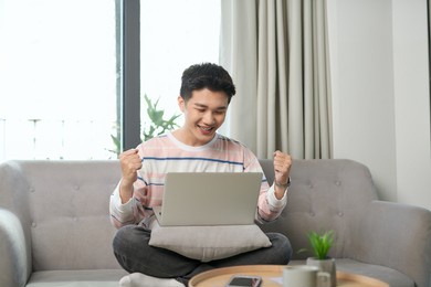 excited young male relax on couch triumph read good news in email or get pleasant response, promotion letter