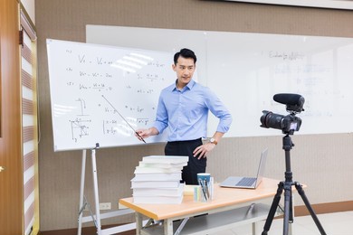 asian senior high school male teacher teach physical online through camera in classroom