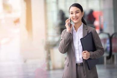 asian woman with smartphone standing against street blurred building background. fashion business photo of beautiful girl in casual suite with phone and cup of coffee