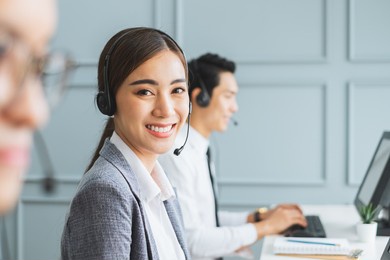 asian call center team, customer service, telesales in formal suit wearing headset or headphone talking with customer in modern office