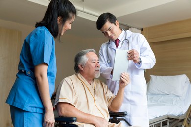 doctors and physical therapists are caring for elderly sick people. doctor and nurse taking care of elderly patient at hospital room. elderly patient using tablet.
