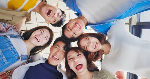 directly below shot of asian young friends forming huddle and their head forming a circle indoor