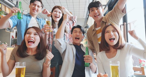 slow motion of asian six friends drinking beer in the restaurant watch ball games on tv and excited with fist gesture 