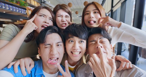 asian young six friends taking selfie and making funny face in restaurant happily