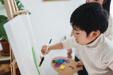 asian kid painting on canvas during art class at home - focus on child eye