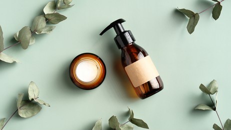 skincare cosmetics products and eucalyptus leaves on green background top view. flat lay jar of moisturizer cream and natural herbal shower gel in amber glass dispenser bottle. spa treatment concept.