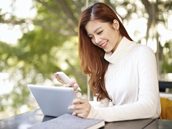 asian young woman working with mobile phone and tablet computer in coffee shop.