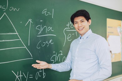 young smiling teacher standing in front of chalkboard