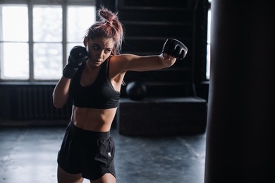 athletic fit female boxer exercising punches with boxing bag in gym during kickboxing and self defense intensive workout