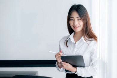 portrait of gorgeous  secretary woman with long curly hair holding tablet standing in meeting room.