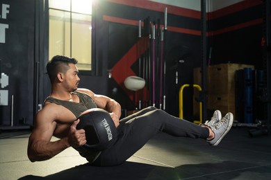 working out at gym concept. young asian handsome man working out his abdominal muscles by holding the medicine twist left and right sitting in the modern loft gym. health and fitness concept.