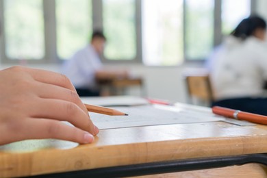 high school or university student reading 
question exam test and using pencil writing on paper answer sheet, lecture chair doing final exam attending in examination classroom with student in uniform
