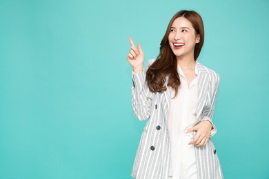 young asian woman smiling and pointing finger to empty copy space isolated on green background