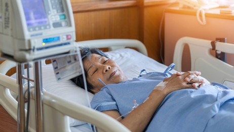 hospitalized elderly patient woman laying on bed in hospital ward room with iv medical infusion pump infusing saline solution fluids, medication for health treatment