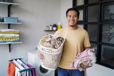 housework. asian man doing laundry at home loading clothes into washing machine