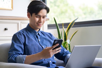 young asian man is using the phone while using the computer
