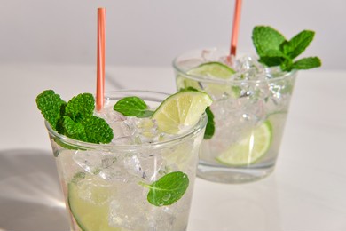 detail of a pair glasses of mojito cocktail on white marble table.