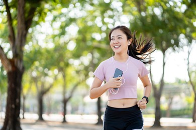 healthy asian woman running in the park in the morning. she smiled joyfully while jogging.