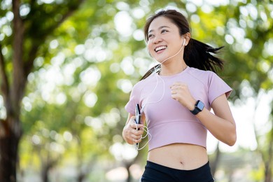 healthy asian woman smiling while running in the park in the morning. she is exercising while listening to music.