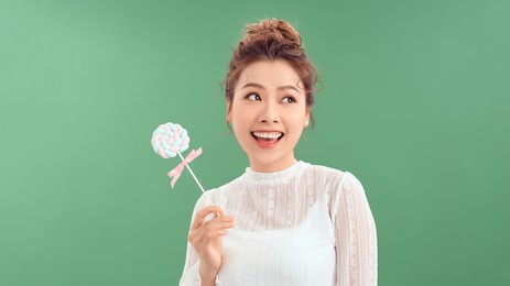surprised curly girl eating lollipop. beauty model woman holding pink sweet colorful lollipop candy, isolated on green background.