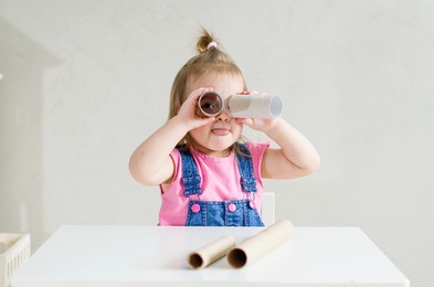 cute little girl looking through a cardboard tube like in a telescope, spy with a cardboard telescope, toilet paper roll for children's activities at home, games for sensory processing disorder