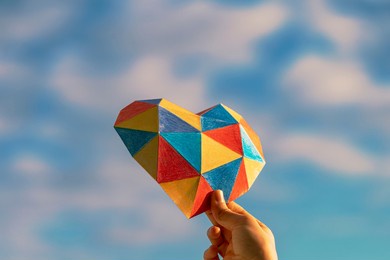 child hands holding colorful heart over blue sky background. world autism awareness day concept