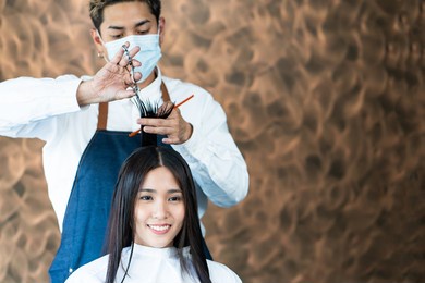 selective focus at face of asian women with hair stylish while do hair cut and wearing surgical face mask while styling hair for client. professional occupation, beauty and fashion service new normal