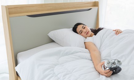 youn and beautiful black long hair asian woman lazy awake from sleeping on bed in bedroom and turn off alarm clock.