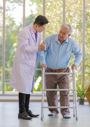 a young male asian doctor wearing white lab coat try to supporting his patient by holding his right arm when an old fat gray hair patient wearing light blue shirt and brown pants standing.