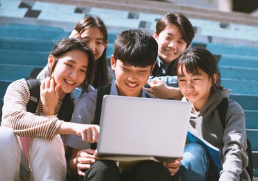 happy young students looking at laptop and sitting on the stairs