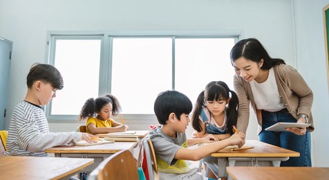 pupil boy hi five with teacher in classroom at elementary school. student boy studying in primary school. children writing notes in classroom. education knowledge, successful teamwork concept