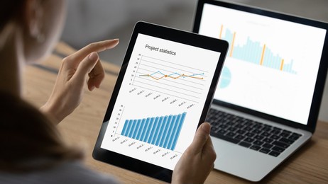 close up back view of female accountant work on electronic gadgets prepare financial report on tablet and laptop. businesswoman use devices manage finances, analyze diagrams statistics in office.