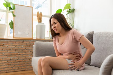 asian woman has a stomach pain. asian young woman has a menstruation and pain period cramps while sitting on the sofa at home. health care concept