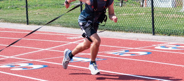 a high school track male track and field athlete is pulling a weighted sled for strength and resistance training on a red track.
