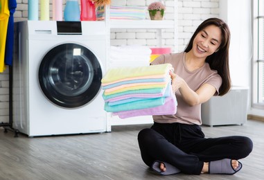 young and beautiful asian woman happy with chore and holding stack of clean and good smell towel chothes.