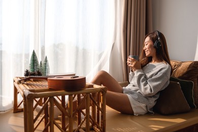 a beautiful young asian woman enjoy drinking coffee and listening to music with headphone at home