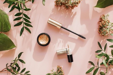 flat lay composition with products for decorative makeup on a pink background. mascara, eyeshadow, eyeliner and green leaves with flowers on a pink background. view from above. beauty background